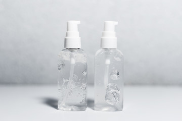 Close-up of two portable plastic bottles with sanitizer antiseptic gel on white table. Grey textured background.