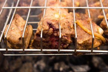 Barbecue of pork with blood on the grill in the process of cooking on an open fire. A piece of pork on the grill with blood juice protruding from it, close-up.
