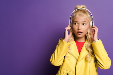 shocked kid with headphones looking away on purple background