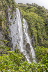 Fototapeta na wymiar tall waterfall on steep slope with lush vegetation, near Whataroa, West Coast, New Zealand