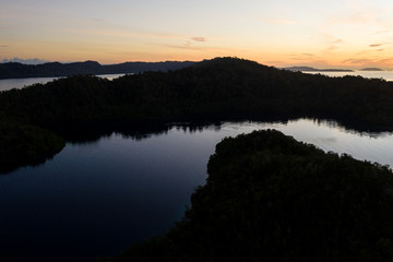 Fototapeta premium A peaceful sunrise illuminates the calm waters within Raja Ampat, Indonesia. This area is known for its incredibly high marine biodiversity and is a popular destination for water lovers.