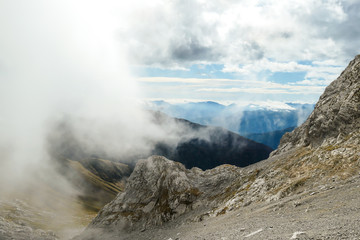 Sharp and rocky mountains range at Austrian-Italian border. There s a path mark on a stone. Serenity and peace. Clouds breaching high mountains. Lots of loose rocks, possibility of landslide