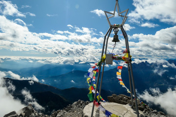 View from the top of Monte Coglians, Hohe Warte on the Austrian-Italian Alpine border. Metal construction with a bell, wrapped with prayer flags waving on the wind. Happiness and achievement. Overcast