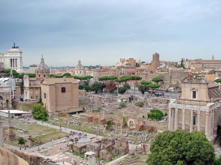 Obraz premium Landscape of millennial columns and dilapidated majestic buildings of mighty Rome in the past, against the backdrop of modern areas under a cloudy sky on the horizon.