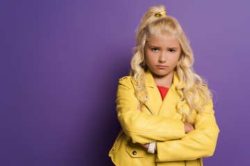 offended kid with crossed arms looking at camera on purple background