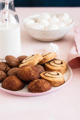 Cookies on a white plate with milk on a pink background.