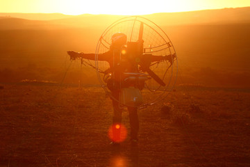 Paramotor pilot taking off on a grass meadow backlit with the sun at a low level.