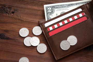 Open leather wallet with dollars and rubles on a wooden table.