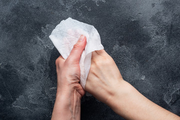 Hands are wiped with a damp antibacterial cloth. The concept of hand cleanliness and the fight against virus microbes. Concrete dark background.