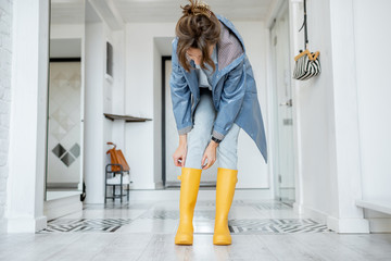 Woman wearing yellow boots and raincoat at the hallway of the apartment. Rainy weather concept