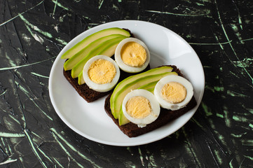 Sandwiches with avocado and egg on a dark background, top view