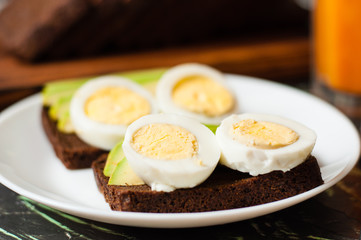 Black whole grain bread, sandwiches with eggs and avocados, multifruit juice in a tall glass. Concept proper nutrition