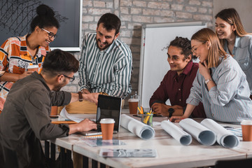 Group of modern business people in casual wear discussing architectural designs while sitting in the creative office.