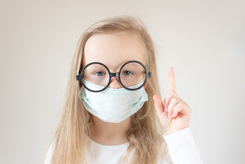 Little blond girl with a medical mask on her face on a white background. Coronavirus protected