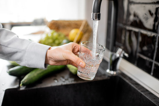 Woman Filling Drinking Glass With Tap Water On The Kitchen. Concept Of Clean Drinking Tap Water At Home