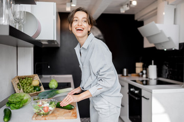 Young and cheerful woman cooking food with healthy vegetarian ingredients on the kitchen at home. Healthy eating, food and lifestyle concept