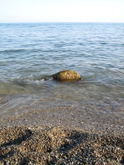 Weak waves gently wash the stones lying on the shallow bottom of the sea rocky shore in good weather.