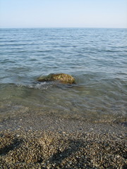Weak waves gently wash the stones lying on the shallow bottom of the sea rocky shore in good weather.
