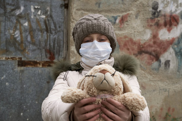 concept of epidemic and quarantine - a gril with a face mask and a cuddly toy alone on the street in the city