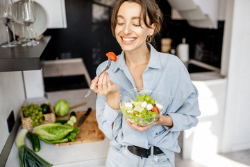 Portrait of a young and cheerful woman eating healthy salad on the kitchen at home. Healthy eating, food and lifestyle concept