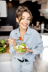 Portrait of a young and cheerful woman eating healthy salad on the kitchen at home. Healthy eating, food and lifestyle concept
