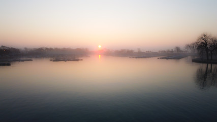 Wide angle shot of calm water in lake inlet with empty boat docks as sun rises over fog covered trees in the early morning in Chicago Illinois