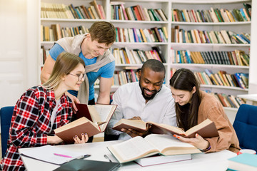 Multiracial young people enjoying group study at table in library. Happy university students sitting together at table with books and laptop for researching information for their project or exams