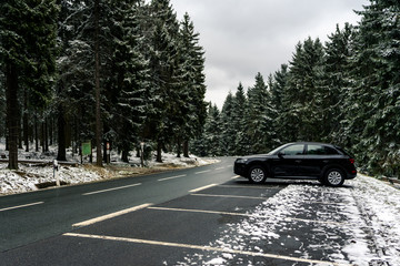 parked car on curved wet asphalt road in snowy pine forest