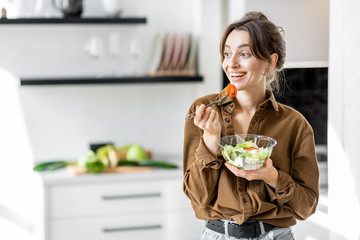 Portrait of a young and cheerful woman eating healthy salad on the kitchen at home. Healthy eating, wellbeing and lifestyle concept