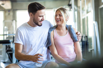 Young caucasian couple at gym talkign together and drinkking water after exercise.