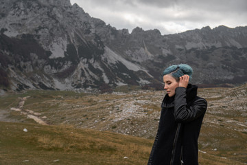 Fototapeta na wymiar A young woman with blue hair in a black coat walks on the mountainside