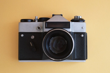 View from the top on vintage film photo camera on the yellow background. Metal silver and plastic black frame with lens.