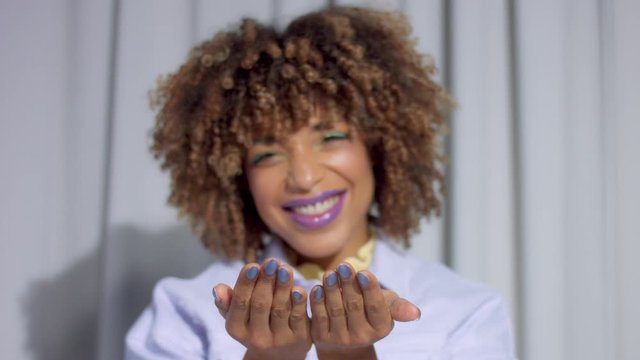 Mixed race happy woman on grey curtains background blow to the hand full of silver glitter toward to camera