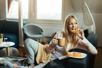 Young woman eating waffles and drinking coffee while relaxing at home.