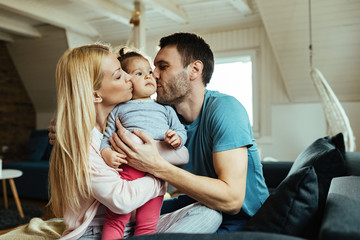 Obraz premium Affectionate parents kissing their small daughter at home.