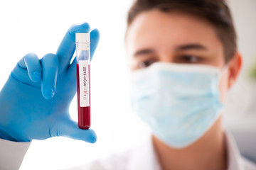 Test tube in male hand close up, doctor in medical mask holding vial with red liquid. Concept blood sample, coronavirus diagnostic, medical research