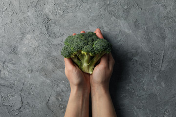 Obraz na płótnie Canvas Female hands hold broccoli on grey background, top view