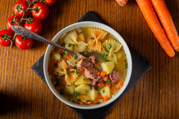 Soup with smoked meat, vegetables and pasta in a white bowl