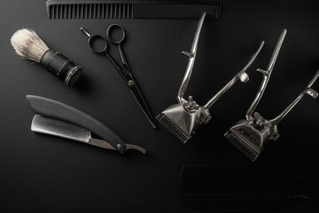 On a black surface are old barber tools. two vintage manual hair clipper, comb, razor, shaving brush, hairdressing scissors. black monochrome.