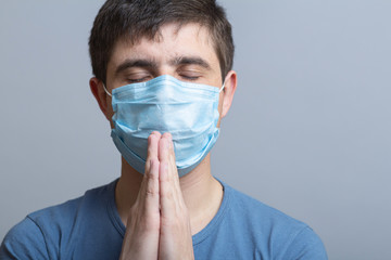 young man in a protective medical mask folded hands near chin and praying to God, doctor on studio backgroung, concept life and religion