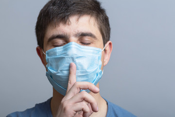 portrait of a man in a protective medical mask on face showing sign of silence gesture putting finger in mouth and lips, concept medical secrecy, moment of mourning and silence