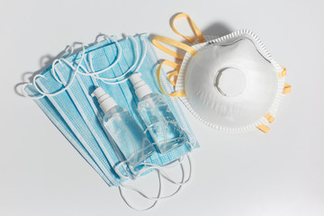 Top view of sanitizer antiseptic gel bottles and respiratory medical flu masks against coronavirus, on white table.