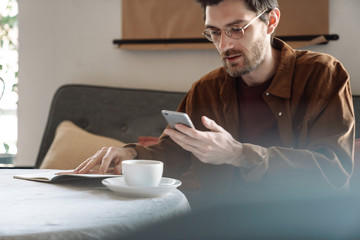 Image of handsome focused young man wearing eyeglasses using cellphone
