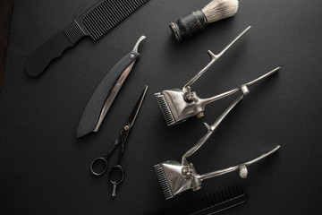 On a black surface are old barber tools. two vintage manual hair clipper, comb, razor, shaving brush, hairdressing scissors. black monochrome. horizontal orientation.