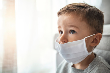 Toddler boy with medical mask on the face. Covid 2019 corona virus outbreak. Sad child isolated on white. Boy at home. Little boy trying to stay healthy by wearing a mask