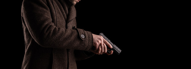 A man in a dark coat holds a gun. Security guard or bodyguard with arms in hand.