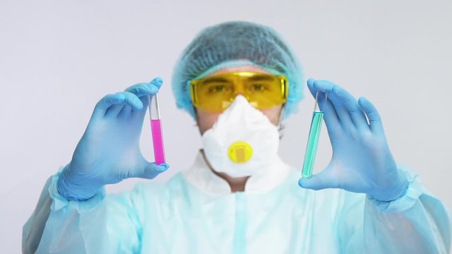 laborant in biohazard suit showing two sample of antivirus to covid-19