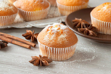 Freshly baked muffins are laid out on the kitchen table on a metal tray and in a plate. Cinnamon sticks and star anise and white sugar are scattered on the table. Sweet dessert.