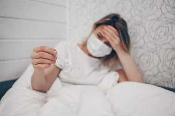 Sick woman lying in bed with thermometer and checking high temperature at home quarantine isolation. Corona virus COVID-19. Infection causes respiratory illness first symptoms cough headache fever
