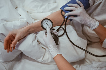 Unrecognizable doctor nurse in medical gloves measures blood pressure with a sphygmomanometer. Coronavirus (COVID-19). First symptoms. Woman sick of flu viral infection in home isolation quarantine
